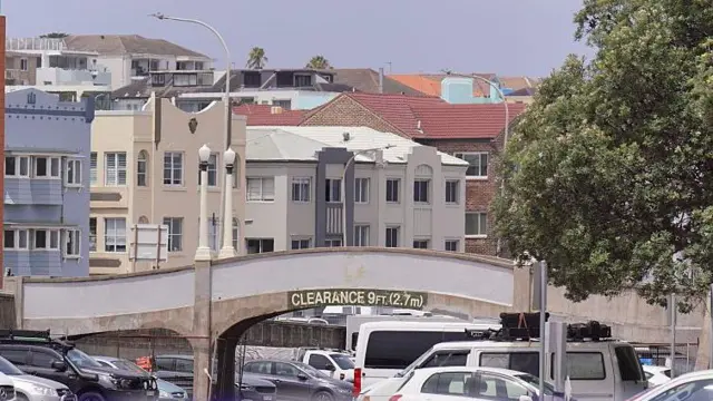 Uma imagem do local do tiroteio que matou 15 pessoas na praia de Bondi, em Sydney, Austrália, mostra uma ponte cinza de 2,7 metros de altura sobre um estacionamento, com prédios ao fundo.